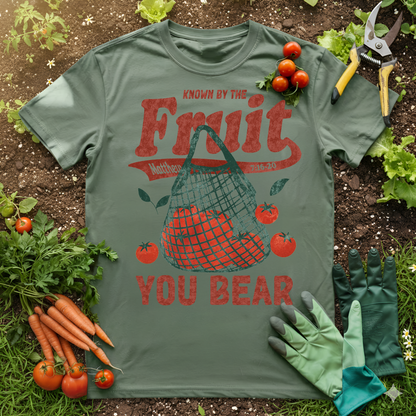 Known by the Fruit You Bear Shirt Christian gardening tee with tomato design in a garden setting.